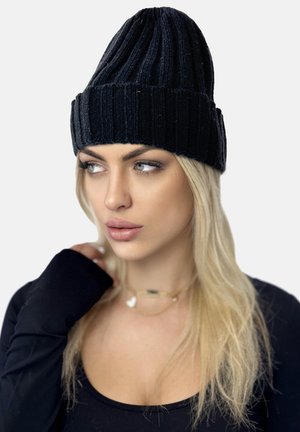 Sort ribbet strikket hue med spidst top og foldet skygge; lavet af blødt, tekstureret stof. Modellen har den på sammen med en sort top.