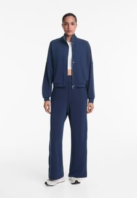 Marinblauer sportlicher Trainingsanzug mit einer kurzen Zip-Jacke mit Stehkragen und weit geschnittenen Hosen mit elastischem Bund. Glatte Textur.