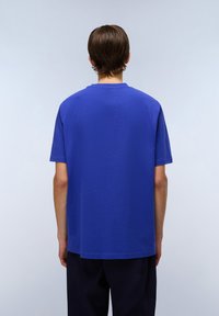 Tričko s krátkým rukávem a kulatým výstřihem v živé modré barvě z bavlny. Má volnější střih s rovním lemem a minimálními švy.