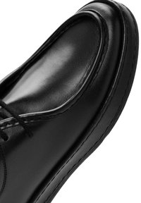 Zapato de cuero negro con acabado suave, punta redondeada y costuras contrastantes. Presenta cordones y un diseño de perfil bajo.