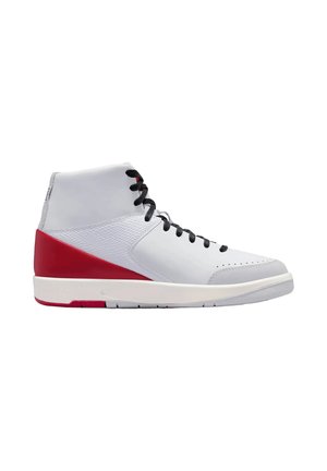 Sneaker alta con parte superiore bianca, pannello sul tallone rosso, lacci neri e suola bianca, mostrata di profilo su sfondo bianco.