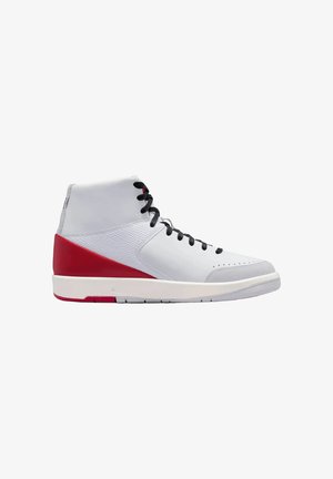 High-Top-Sneaker mit weißem Obermaterial, rotem Fersenbereich, schwarzen Schnürsenkeln und weißer Sohle, von der Seite auf weißem Hintergrund gezeigt.