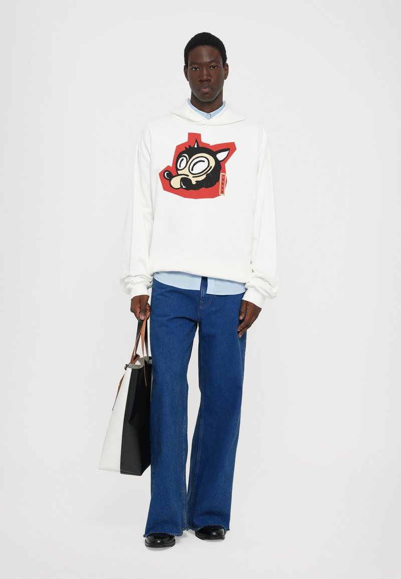 Hvid hættebluse med et farverigt tegneserie-dyr grafik, parret med blå løse jeans og en sort-hvid taske.