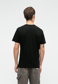 Melna kokvilnas T-kreklu ar apaļu kakla izgriezumu un īsām piedurknēm, ar gludu tekstūru. Aizmugurējā skatā ir vienkāršs dizains bez grafikām.