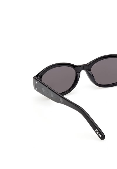 Czarne owalne okulary przeciwsłoneczne z ciemnymi soczewkami, z ozdobnymi zausznikami i logo "MCM" na lewym zauszniku.