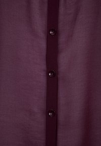 Burgundy knap-shirt med en glat, vævet tekstur, fem mørke knapper nedad langs fronten og en simpel krave.