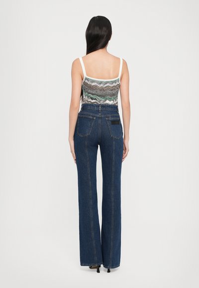 Vue arrière d'une personne portant un débardeur à motif zigzag avec des fines bretelles et un jean en denim bleu foncé à taille haute et jambes larges.