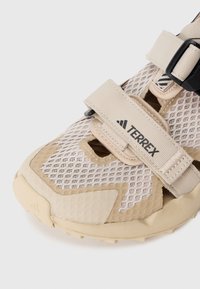 Sandalia de malla transpirable beige con correas de Velcro y una suela de goma texturizada. Presenta la marca Terrex y recortes para ventilación.