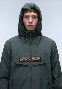 Grønne lynlåsjakke med hætte, med et forreste logo-patch, tekstureret stof og justerbare snore i hætten for bedre pasform.