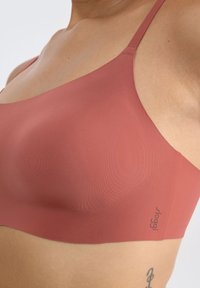 Roze draadloze bh van gladde, rekbare stof met minimale naden. Logo aan de zijkant en dunne verstelbare banden.
