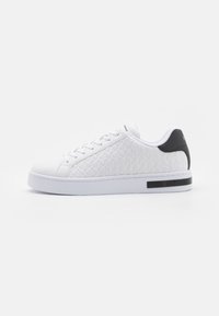White sneakers with a textured upper featuring a geometric pattern, round toe, flat white sole, and a black heel accent.