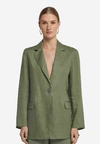 Olivgrön linneblazer med kavajslag, enstaka knappstängning och två framfickor; slät textur och avslappnad passform.