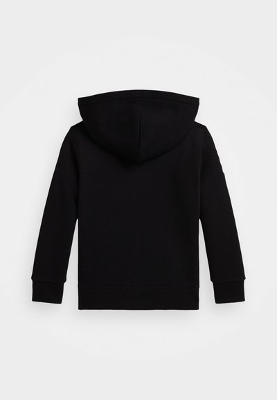 Melnā kapuce, kas izgatavota no mīkstas auduma, ar lielu kapuci, garām piedurknēm un ribotām aprocēm. Gluda tekstūra bez redzamām rakstām vai akcentiem.