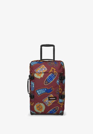 Rolling suitcase with a maroon fabric featuring colorful patches, including logos and text. It has a retractable handle and buckles.