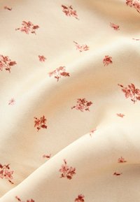 Tissu crème avec de petits imprimés floraux roses épars et de doux plis créant des ombres douces et de la texture.