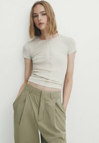Un top court côtelé beige clair à manches courtes, avec une couture centrale. Associé à un pantalon ample taille haute vert olive.