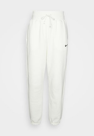 Bele trenirke iz mehkega blaga, z elastičnim pasom in vrvico za zategovanje, stranskimi žepi ter črnim Nike logotipom na levem stegnu.