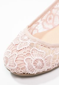 Ballerines en dentelle rose pâle avec un motif floral, bout rond et doublure intérieure douce. Elles présentent un fin galon élastique autour de l'ouverture.
