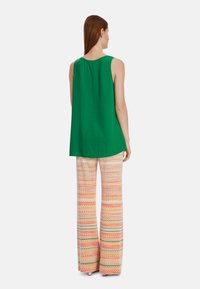 Green sleeveless top with a rounded neckline, paired with wide-legged pants featuring a multicolored zigzag pattern and textured fabric.