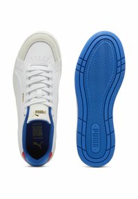 Sneakers bianchi con una parte superiore in pelle liscia, accenti blu intorno al colletto e una suola in gomma blu testurizzata con il logo PUMA.