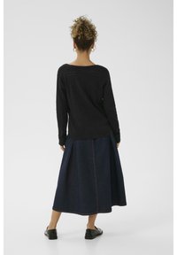 Maglione nero lavorato a maglia con un retro testurizzato, abbinato a una lunga gonna in denim scuro con una cucitura visibile. Scarpe basse nere completano il look.