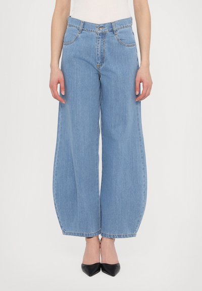 Light blue wide-leg jeans with a high waist, front pockets, and stitched detailing. Worn with black pointed-toe heels.