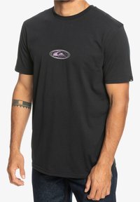 Svart bomull T-shirt med en rund grafisk design i lila och vitt på bröstet. Korta ärmar och rund halsringning.