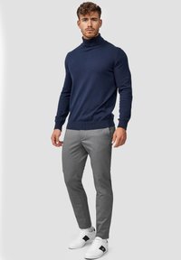 Marineblå høyhalset genser, slim-fit grå bukser og hvite joggesko med svarte detaljer. Glatte teksturer, skreddersydd design og moderne silhuett.