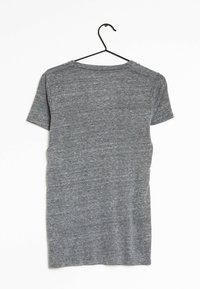 Camiseta gris de manga corta hecha de una tela suave y texturizada, con un cuello redondo y un diseño sencillo, colgando de un gancho negro.