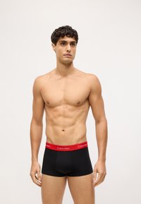 Crne bokserice s kratkim nogavicama i crvenim remenom s logotipom Calvin Klein; glatka tkanina, uski kroj.