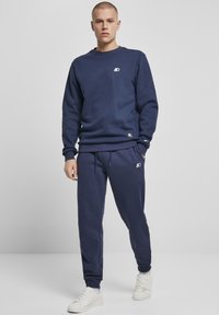 Marineblå sweatshirt og matchende joggers lavet af blødt stof, med et lille logo og ribbet manchetter. Fuldført med hvide sneakers.