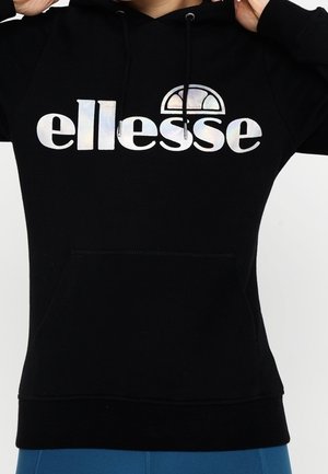 Black hoodie with a metallic "ellesse" logo on the chest, worn by a person adjusting the hood strings.