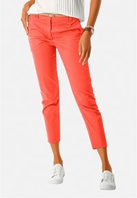 Pantalon court corail en coton léger avec une texture lisse, associé à des baskets blanches. Comprend une ceinture et des poches avant.