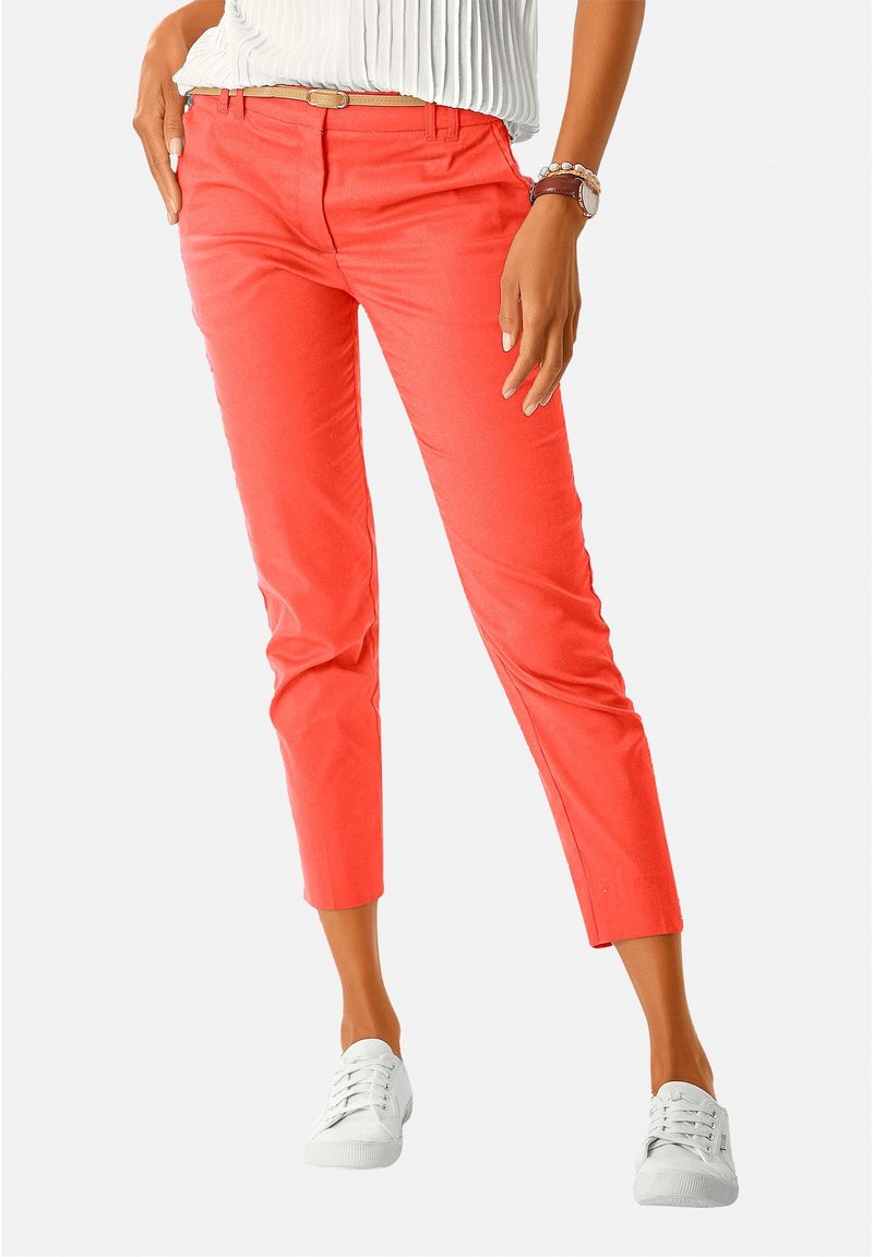 Pantalon court corail en coton léger avec une texture lisse, associé à des baskets blanches. Comprend une ceinture et des poches avant.