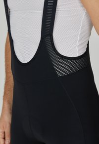 Schwarze Fahrradhose mit Trägern aus Mesh und gepolstertem Gesäß; zeichnet sich durch nahtloses Design, enganliegenden Schnitt und atmungsaktiven Stoff aus.