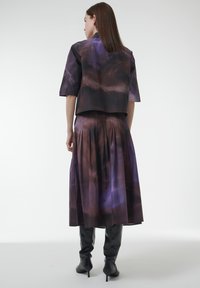 Conjunto de tela fluida en negro y morado con un top corto y una larga falda plisada. Textura suave y diseño de patrón abstracto. Botas negras hasta los muslos.