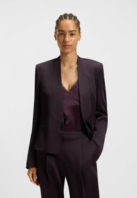Mørkeblå skræddersyet blazer med sjalskrave, parret med en matchende silke-camisole med blondedetaljer. Glat tekstur, minimalistisk design.