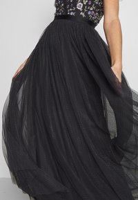 Schwarzes Tüllkleid mit einem bestickten Oberteil und floralen Details, einer taillierten Taille und einem fließenden, geschichteten Rock für Textur.