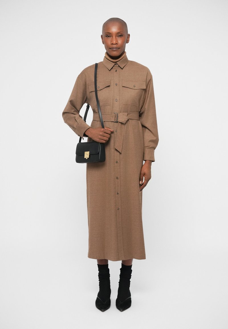 Abito camicia marrone, maniche lunghe, con chiusura a bottoni, due tasche sul petto, vita cin cin, abbinato a una borsa crossbody nera e calze nere.