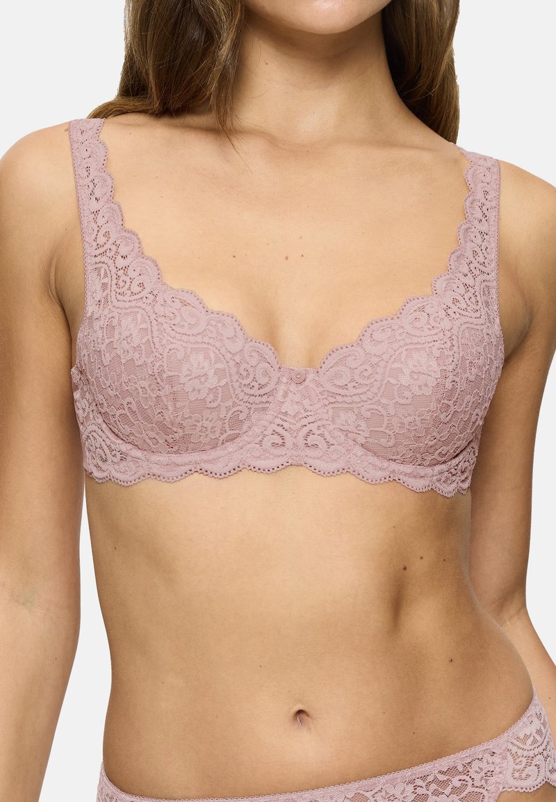 Kant bralette in zacht mauve met geschulpte randen. Bevat een delicaat bloemenpatroon en verstelbare banden, wat zorgt voor een naadloze uitstraling.