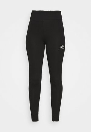 Leggings noirs avec une taille haute, texture lisse et un accent de logo blanc sur la cuisse gauche. Coupe ajustée et matériau extensible.