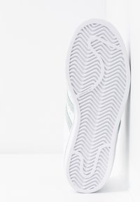 White sneaker sole with textured surface; features zigzag pattern. Side displays green accent and discrete branding near the heel.