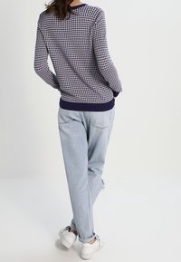 Pull en motif bleu marine et blanc à manches longues, associé à un jean droit bleu clair et des baskets blanches, vu de dos.