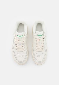 Beli usnjeni športni čevlji s kremnimi detajli, okroglo konico, vezalni sprednji del, oblazinjen ovratnik in Reebok logo v zeleni barvi na ježku.