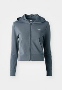 Sudadera con cremallera gris hecha de tela suave, con capucha, bolsillos delanteros y un pequeño logo en el pecho izquierdo. Diseño ajustado, puños acanalados.