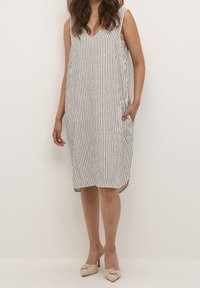 Vestido sin mangas a rayas en blanco y azul marino, diseño con cuello en V, forma fluida, hasta la rodilla, con bolsillos laterales, fabricado en tejido ligero.