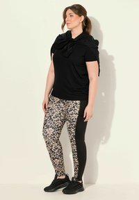 Musta lyhythihainen paita, jossa on nauhatyyny, ja kuviolliset legginssit, joissa on leopardikuvio ja mustat sivupaneelit; yhdistetty mustiin lenkkareihin.