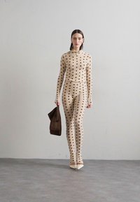 Completo in maglia beige con pois, composto da due pezzi con maniche lunghe e pantaloni attillati, abbinato a una borsa marrone e scarpe chiare.
