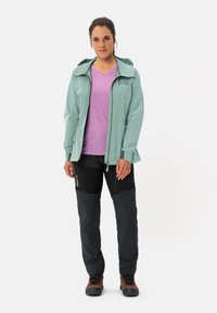 Light green waterproof jacket with a hood, paired with a purple t-shirt and black pants. Features include zippers and sturdy hiking boots.