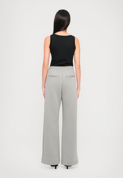 Black sleeveless top paired with wide-legged gray sweatpants featuring an elastic waistband and two back pockets. Smooth texture, relaxed fit.